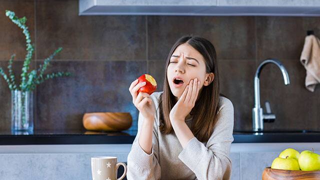 Una mujer joven con dolor de dientes mientras sostiene una manzana