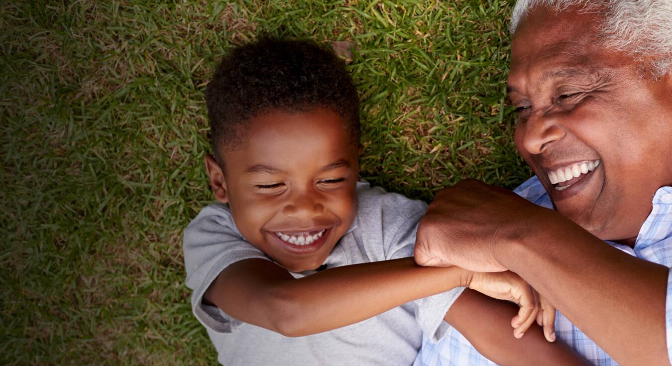 a grandfather and his grandchild smiling brightly laying on the grass