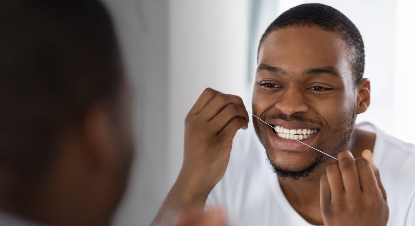 man flossing his teeth in front of the mirror
