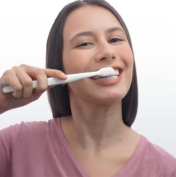 Mujer cepillándose los dientes con pasta dental Colgate Total, mostrando su rutina de higiene bucal para mantener una sonrisa saludable.