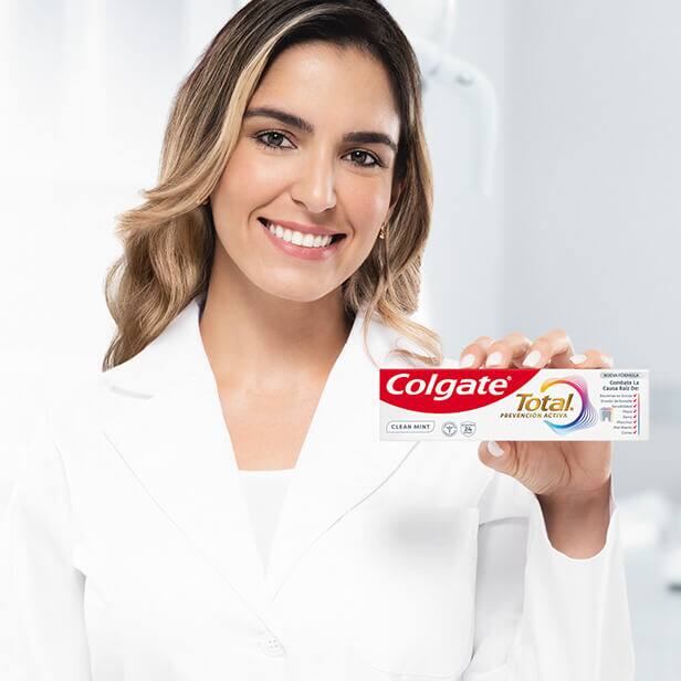 Dentista sonriente sosteniendo un paquete de pasta dental Colgate Total, representando la recomendación profesional del producto.