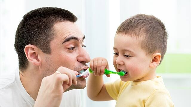 father and son are brushing teeth together