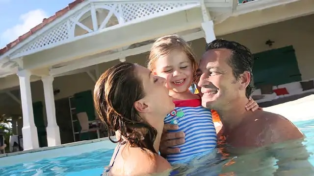 A smiling couple holding a child in a pool