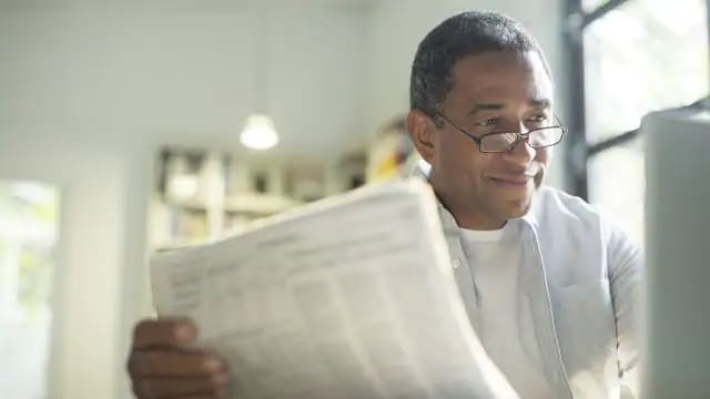 A man with glasses is reading newspaper