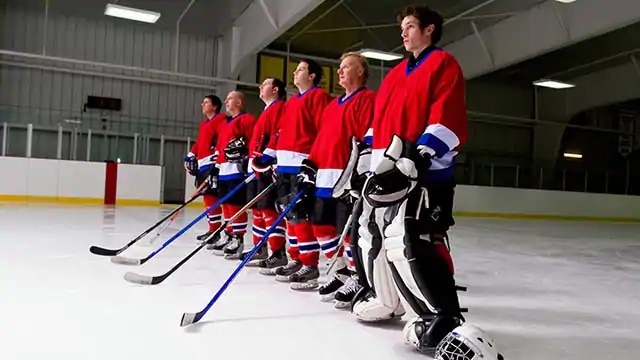 6 male ice hockey players with full gear on are standing in the rink