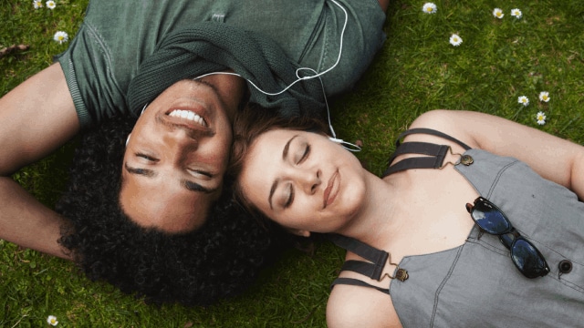 Young couple listening to music while laying on the grass