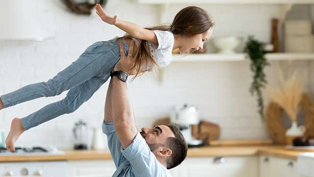 Happy smiling dad lifting his daughter in the air while in the kitchen