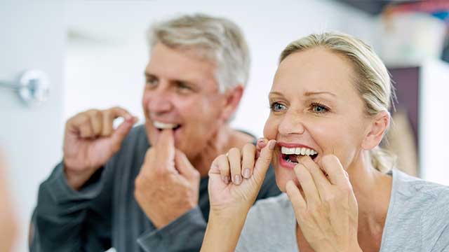 close-up of an older couple flossing their teeth in the bathroom