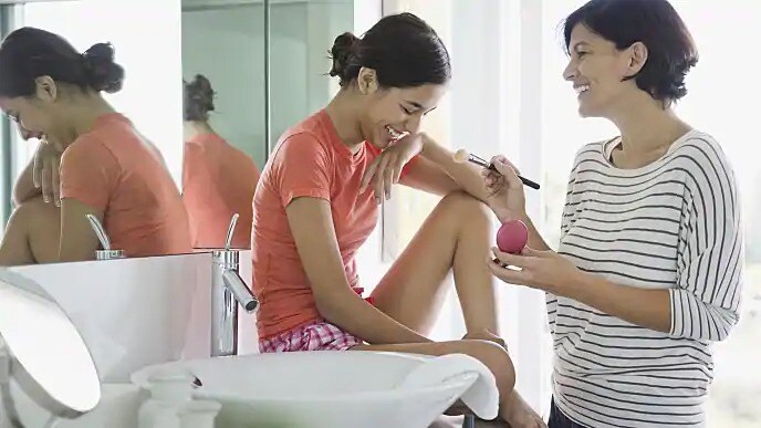 Two women with bright teeth smiling while applying make up