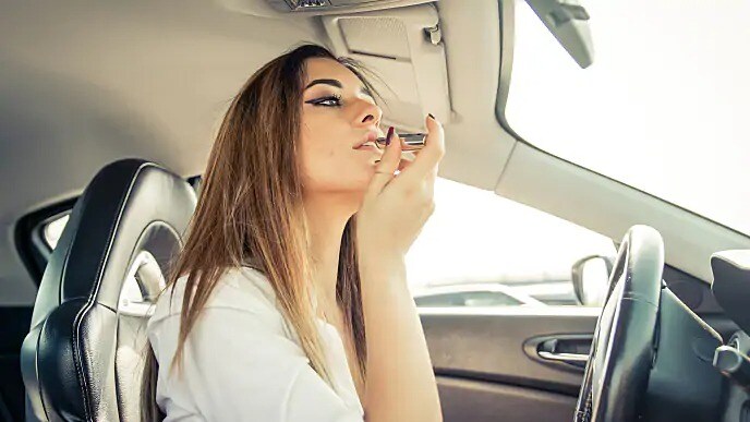 Woman applying lipstick in her rear view mirror