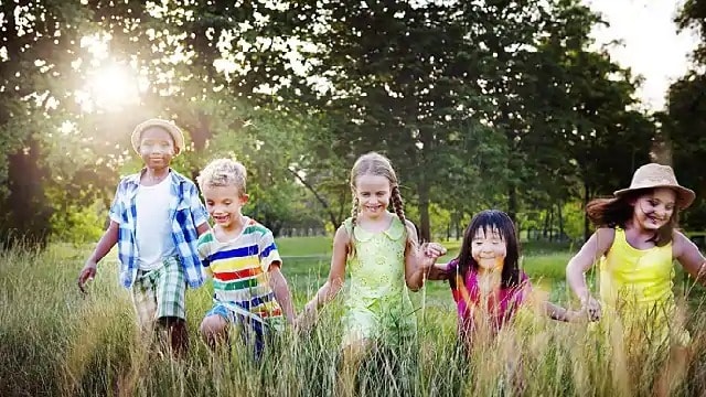 Group of children holding hands walking through grass