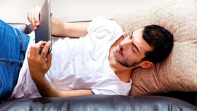 A man looking at a laptop while lying on his back
