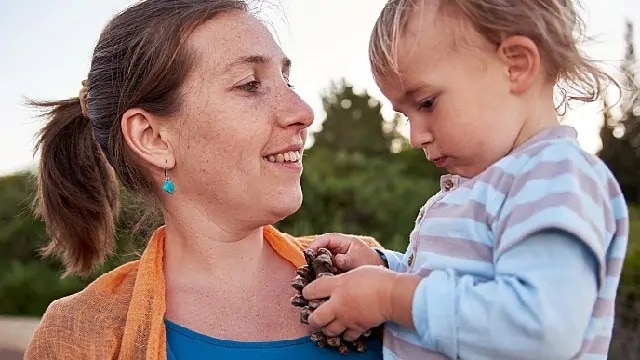 Toddler holding a pine cone while being held by a smiling woman
