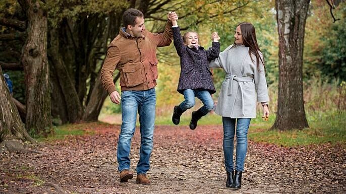 A man and woman walking while lifting a young girl up by the arms