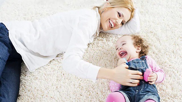 Smiling woman tickling a toddler on the floor