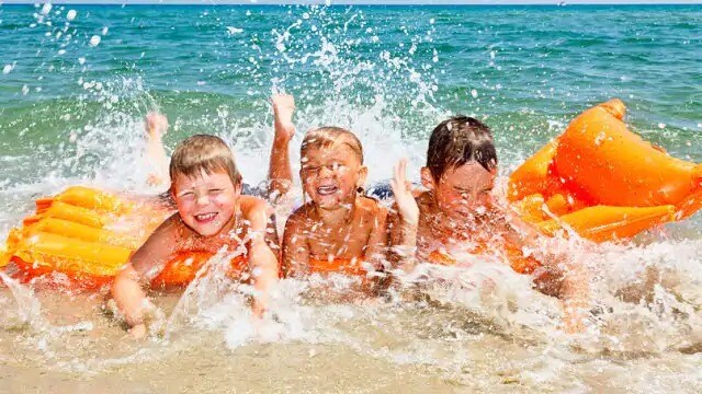 Three children splashing in water at the beach