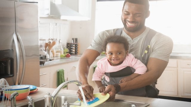 Father holding his infant daughter as they wash the dishes