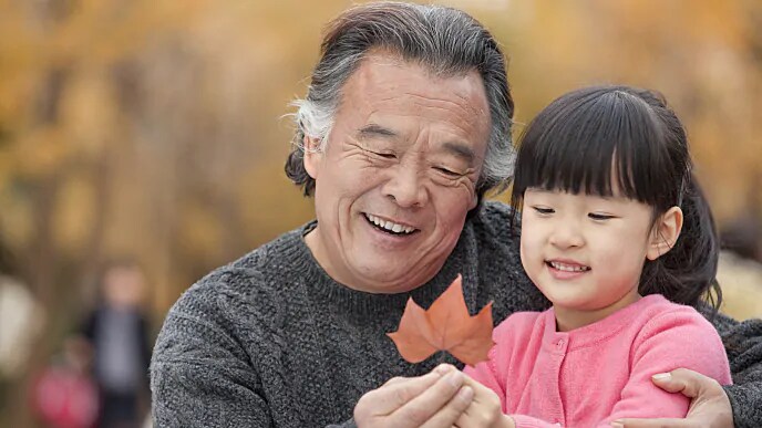 A smiling grandfather looking at a leaf with is granddaughter