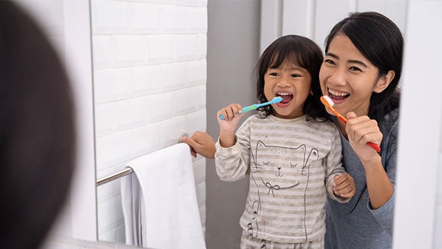 happy mom and kid brushing their teeth together in bathroom sink in the morning