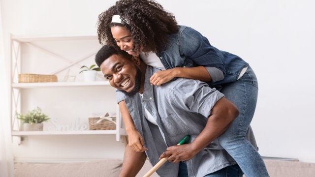 man is giving a piggyback to woman in living room man is giving a piggyback to woman in living room