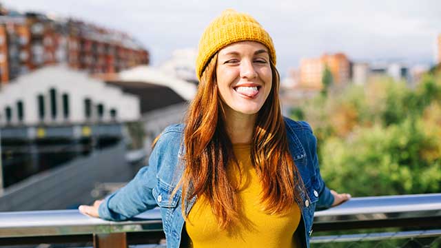 portrait of smiling young woman wearing yellow cap sticking out tongue