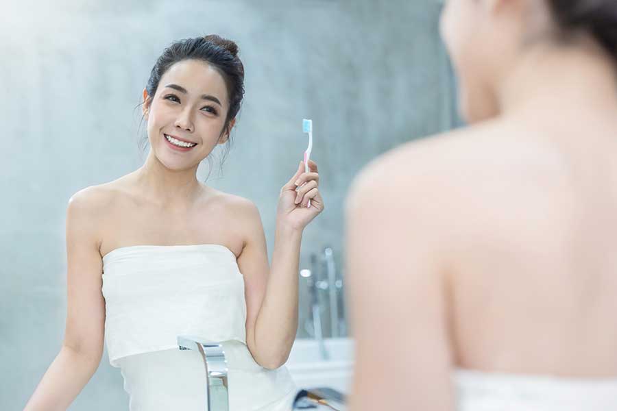 Portrait of young woman holding her toothbrush in front of bathroom mirror