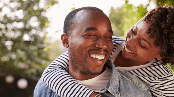 smiling young couple where one is piggybacking on the other person in a garden, eyes closed