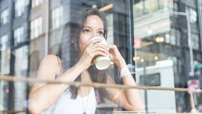 a young lady drinking coffe at a cafe and looking out a window