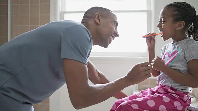 father helping child brush teeth