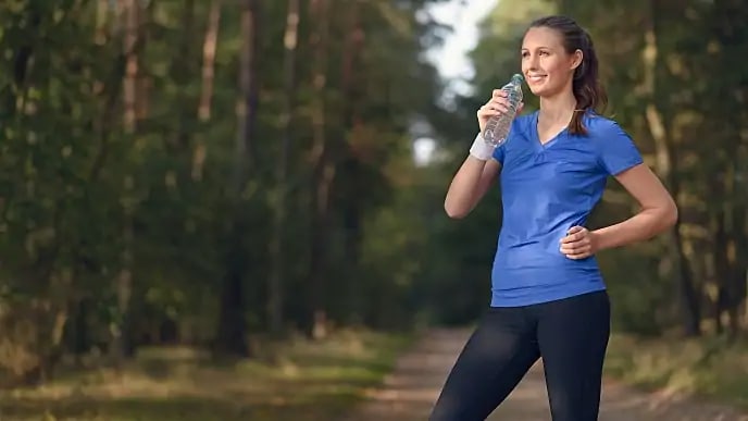 A smiling woman about to drink form a bottle of water