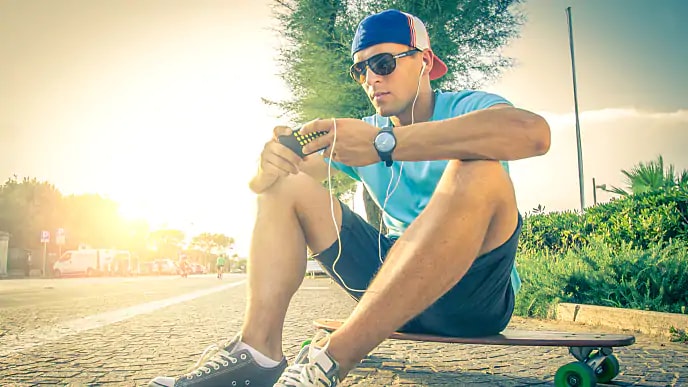 a man is sitting on skateboard and playing on his mobile phone