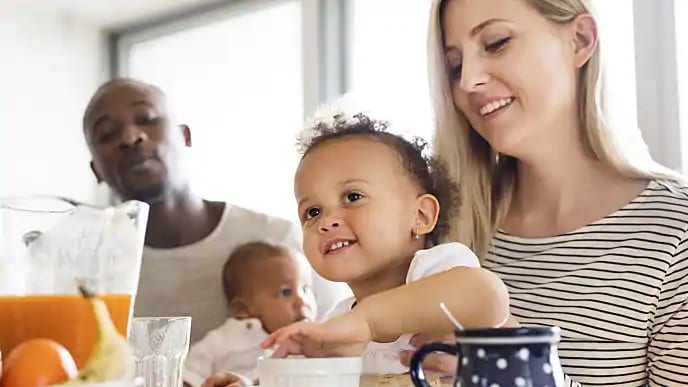 A smiling couple, each holding small children during breakfast