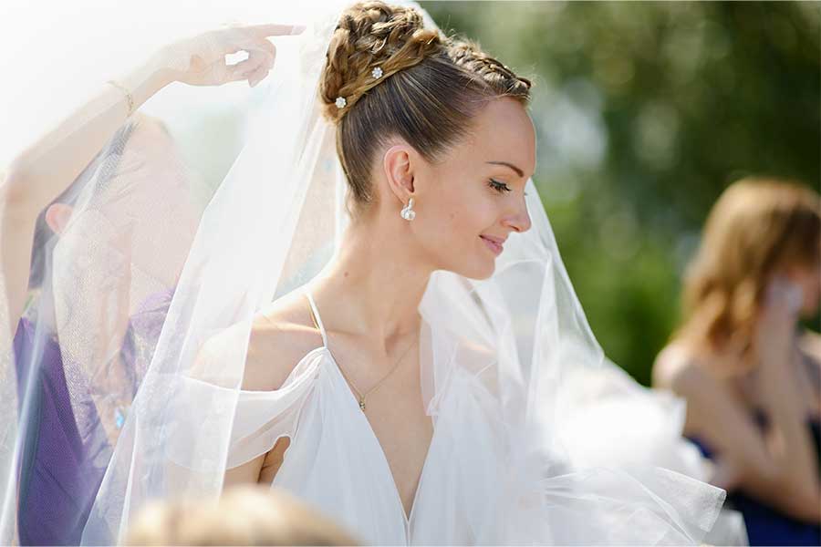 A bride is getting her veil fixed as she stands outside on her wedding day A bride is getting her veil fixed as she stands outside on her wedding day