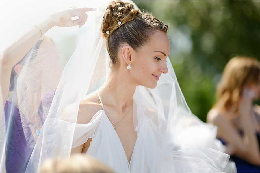 A bride is getting her veil fixed as she stands outside on her wedding day