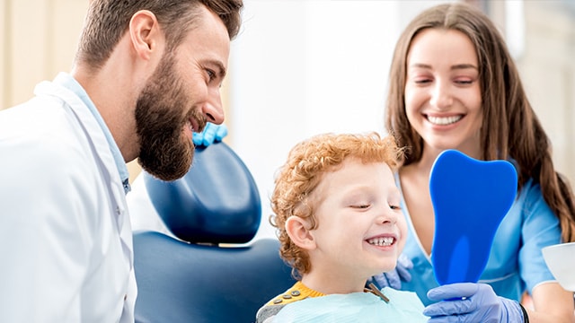 Young boy looking at the mirror with dentist and assistant at the dental office