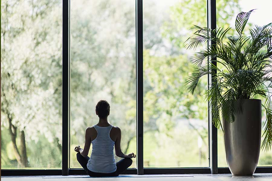 Young woman meditating at home while facing big windows 