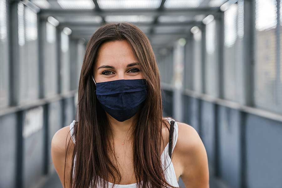 Portrait of  woman standing on an iron bridge in the city with face mask on for protection 