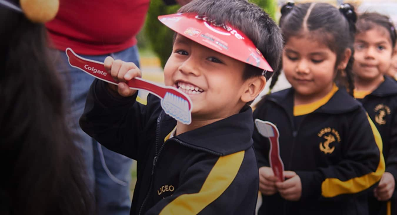 Smiling boy holding a Colgate toothbrush cardboard cutout