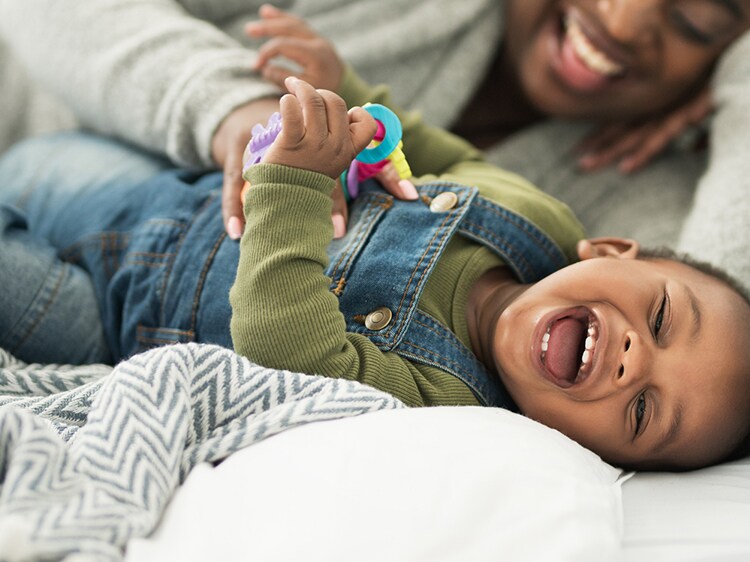 woman tickling toddler on a bed
