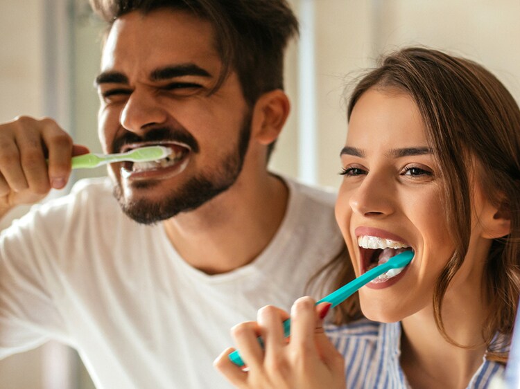 couple brushing their teeth in a mirror