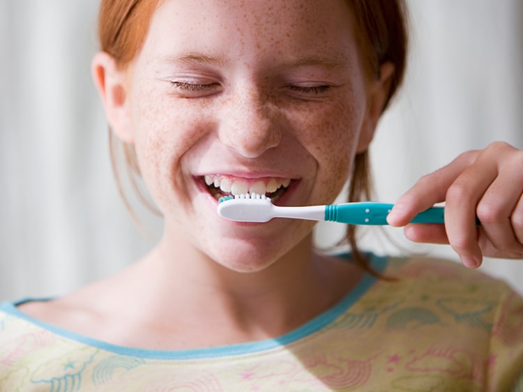 Young girl smiling and brushing her teeth with her eyes closed