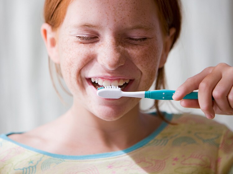 Young girl smiling and brushing her teeth with her eyes closed