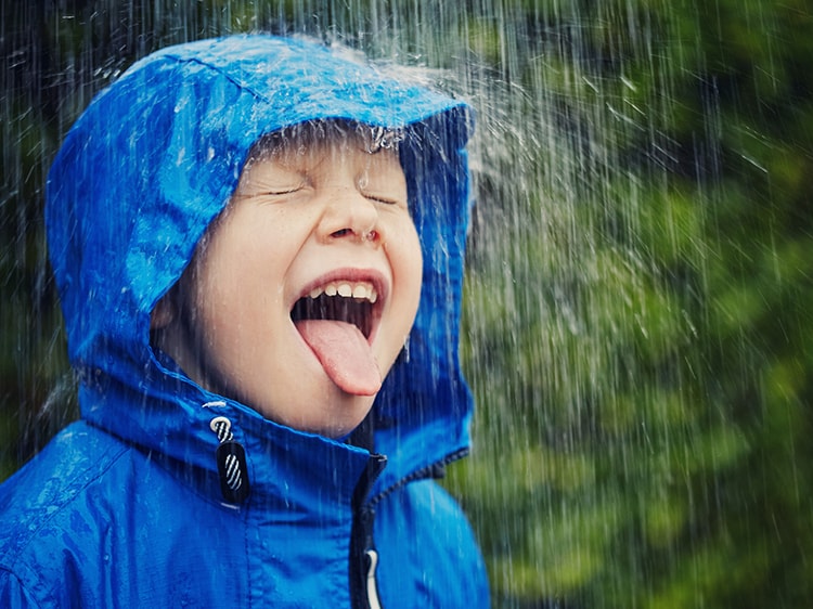 smiling child in a rain coat tasting rain water