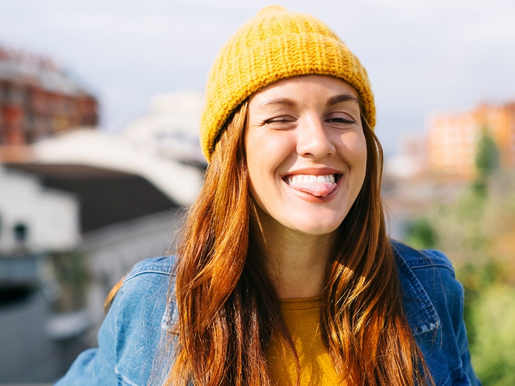 Portrait of young woman sticking tongue out while wearing a yellow beanie and sweater