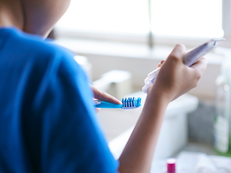 child squeezing colgate toothpaste onto toothbrush