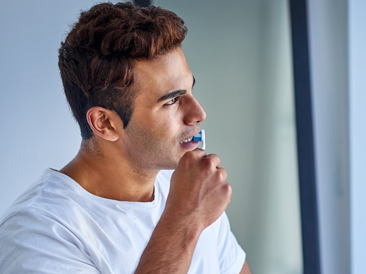 man brushing his teeth with colgate toothbrush