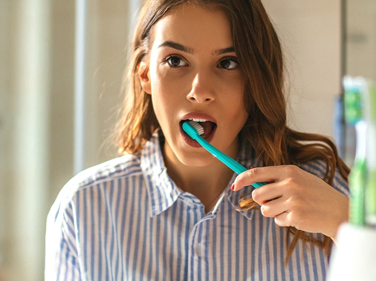 A woman in a striped shirt brushing her teeth in the bathroom mirror