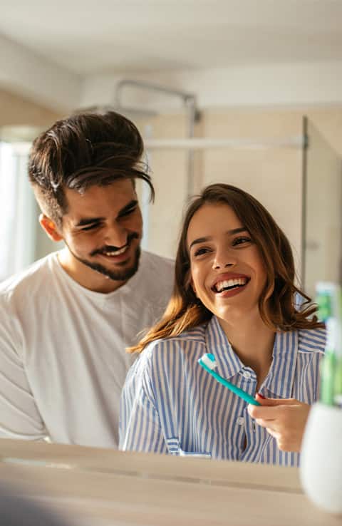 pareja sonriendo mientras usa cepillos de dientes colgate