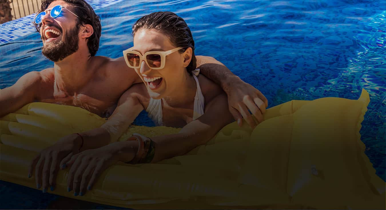 a man and a woman wearing sunglasses smiling in the pool holding a floating device