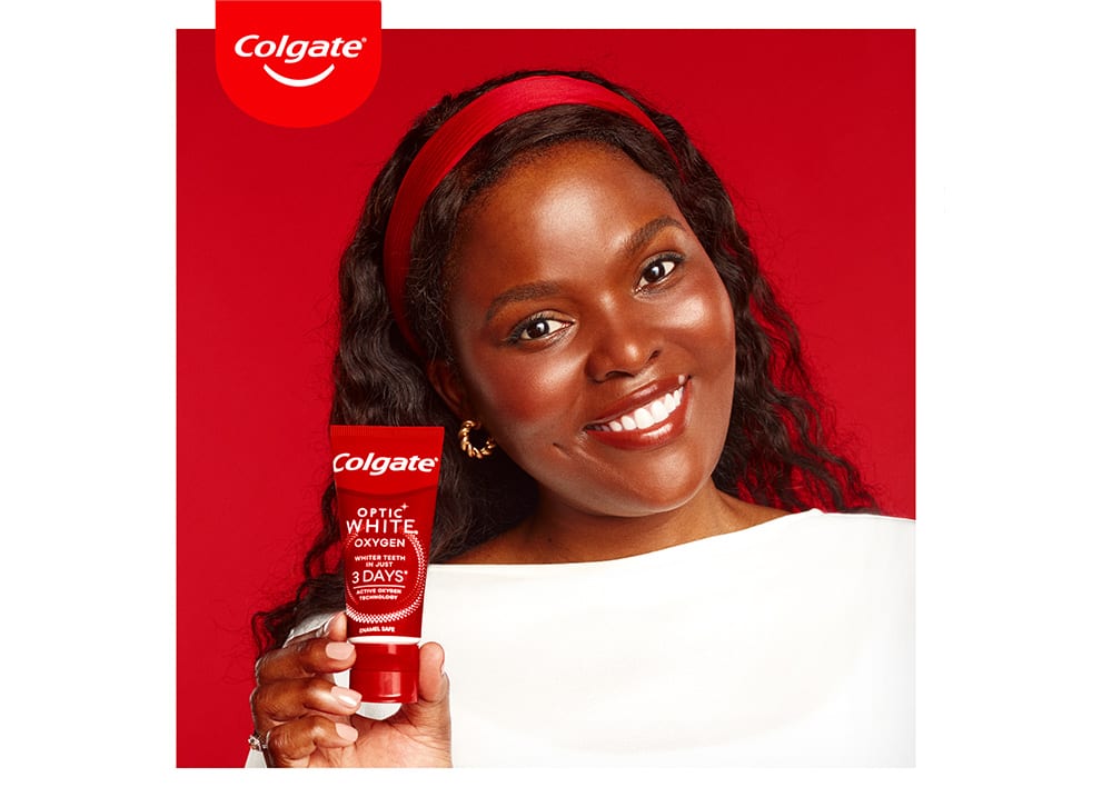 African woman smiling while holding Optic white oxygen toothpaste